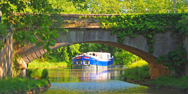 Summer plans - French Hotel Barge Enchante approaching pretty bridge on the canal du midi in the south of France